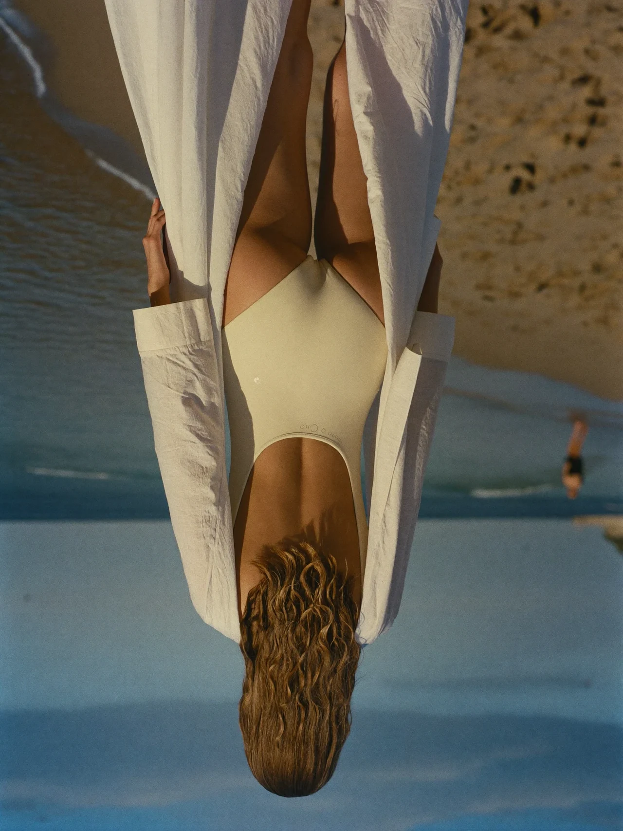 Spiaggia mediterranea al tramonto, figura di spalle in costume e copricostume leggero