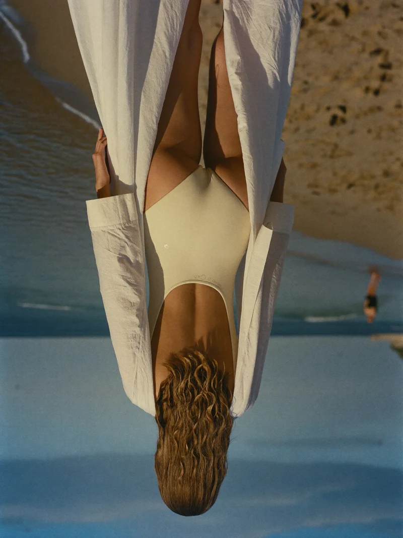 Spiaggia mediterranea al tramonto, figura di spalle in costume e copricostume leggero