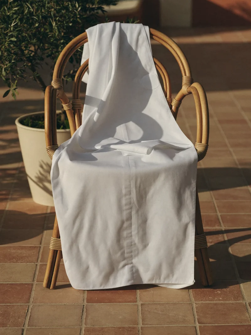 Kaftan in cotone bianco appoggiato a una sedia in rattan su una terrazza